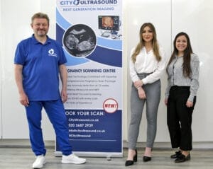 Three members of the City Ultrasound team standing beside a clinic banner